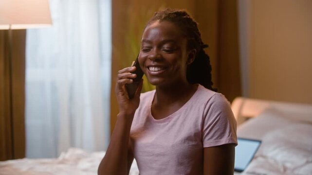 Happy African American woman talking smartphone call at home bedroom night laughing cheerful female friendly relaxed girl student working online laptop chatting conversation mobile phone telling story
