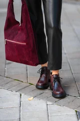 Burgundy suede handbag beside black leather pants and lace up boots on city sidewalk, creating modern urban fashion street style with rich textures and confident color contrast © flywish