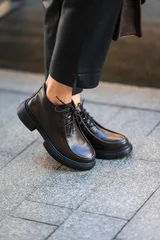 black leather ankle boots standing on urban pavement in casual and stylish fashion setting close-up of feet with gray trousers and clean background copy space for editorial use. © flywish
