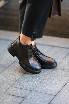 black leather ankle boots standing on urban pavement in casual and stylish fashion setting close-up of feet with gray trousers and clean background copy space for editorial use.
