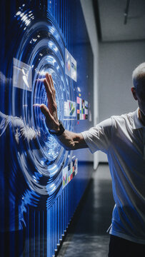 Man reaches toward circular blue glowing ripples on an interactive digital display wall in a dark room. Concentric wave patterns shimmer across the smooth screen surface.