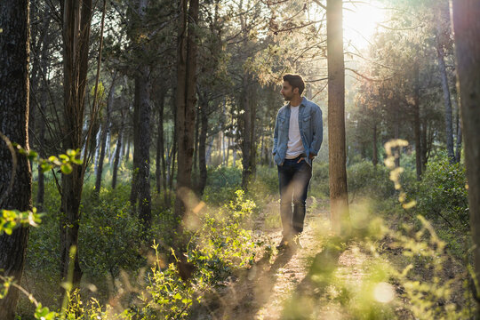Young man standing in forest, against the sun