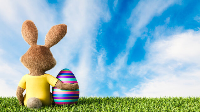 Easter bunny sitting on grass with arm around Easter egg