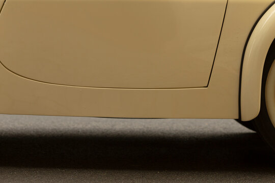 Tight view of a beige car's lower side panel showing the smooth painted surface, fuel door outline and curved wheel arch above a dark asphalt surface; soft