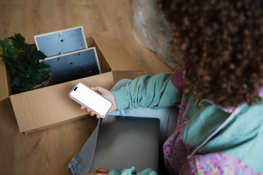 Woman with smartphone and laptop unpacking at home during move