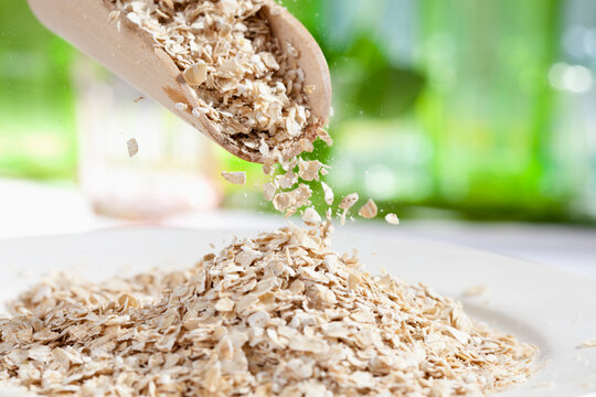 Oat flakes pouring from wooden scoop, close up