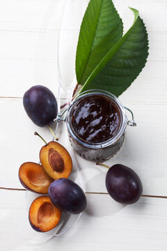 Glass of plum jam and some plums on plastic spoon, studio shot