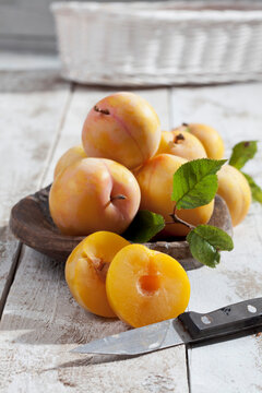 Sliced and whole yellow gages (Prunus domestica subsp. italica) and a wooden spoon on white wooden table, studio shot