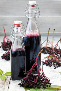 Elderberries (Sambucus) and two bottles of elderberry juice on white wooden table, studio shot