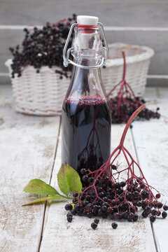 Elderberries (Sambucus), basket and a bottle of elderberry juice on white wooden table, studio shot
