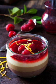 Glass of pudding with vanilla sauce and raspberry sauce garnished with raspberries and orange zest