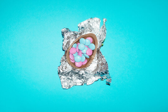 A chocolate easter egg contains colorful candy on a blue background