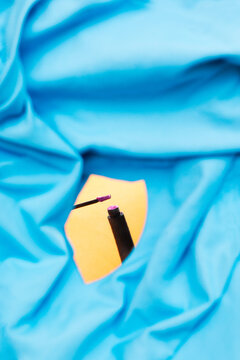 A makeup wand reflects in an orange mirror through blue fabric