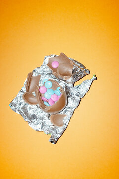 A broken chocolate Easter egg reveals candy on an orange background