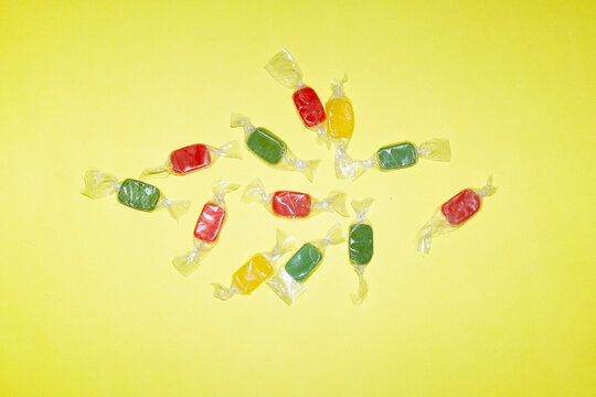 Colorful wrapped hard candy scattered on a bright yellow background