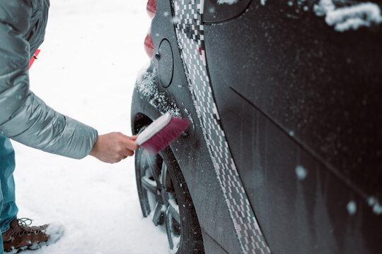 Close-up of a person clearing fresh white snow off an automobile front window and wipers after blizzard. Winter vehicle maintenance, automotive care, and freezing weather concept.