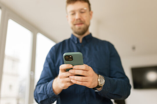 Handsome male smiling while using a mobile phone for texting indoors
