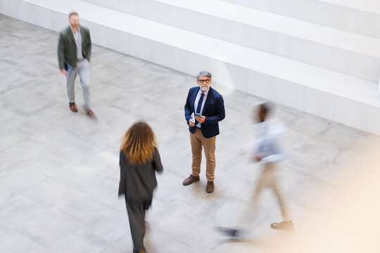 Focused businessman stands still in a busy modern office lobby