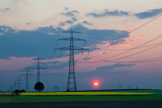 Germany, Bavaria, View of electricity pylon in rapeseed field at sunset