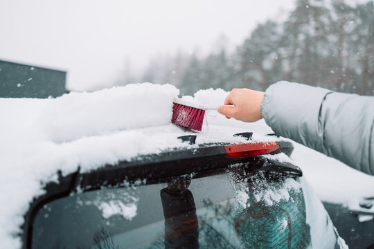Close-up of a person clearing fresh white snow off an automobile front window and wipers after blizzard. Winter vehicle maintenance, automotive care, and freezing weather concept.