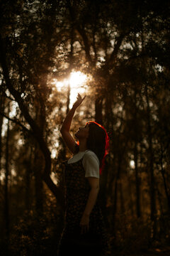Woman reaches her hand towards sunlight in a dark forest