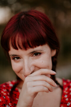 Smiling woman with red hair covering her mouth outdoors