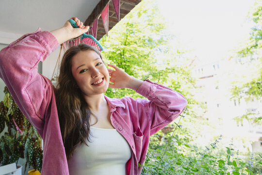 Smiling woman brushes her hair on a tiny green balcony