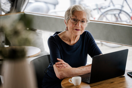 Senior woman sitting at caf� table with laptop smiling and looking at camera