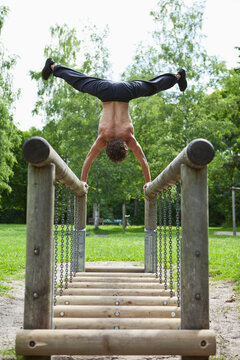 Germany, Bavaria, Young man doing handstand on railing