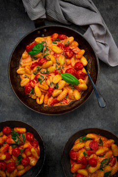 A cast iron pan holds fresh gnocchi with tomato and spinach