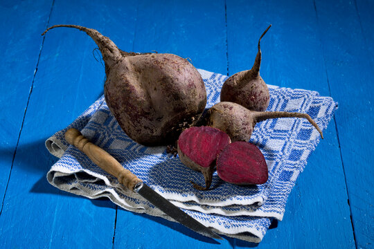 Sliced and whole beetroots (Beta vulgaris), cloth and knife on blue wooden table