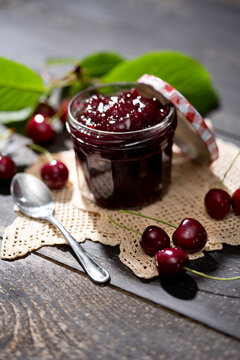Jar of cherry jam, sour cherries and spoon on dolly and dark wood
