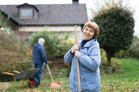 Senior woman smiles while raking autumn leaves in the garden
