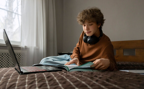 Teenage boy reads a textbook on his bed at home