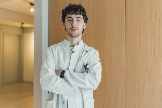 A male junior doctor stands confidently in a hospital hallway