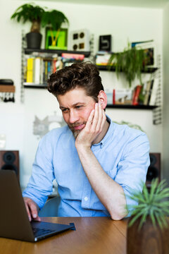Smiling freelancer is reading on a laptop in his home office
