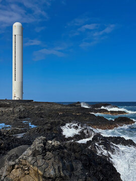 Punta del Hidalgo Lighthouse rising above rugged volcanic rocks on the Atlantic coast of Tenerife, Canary Islands, Spain. A striking coastal landscape with crashing waves and basalt formations