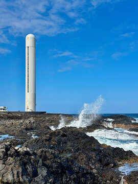 Punta del Hidalgo Lighthouse rising above rugged volcanic rocks on the Atlantic coast of Tenerife, Canary Islands, Spain. A striking coastal landscape with crashing waves and basalt formations