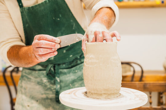 A male artisan shapes a clay pot on a wheel in a workshop