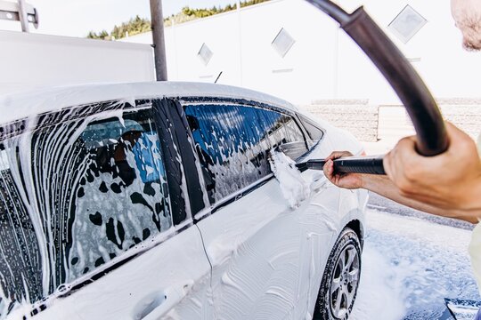 A man washes a white car with a brush and foam at a carwash