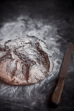 Rye-Spelt-Malt loaf, flour and bread knife on wooden table