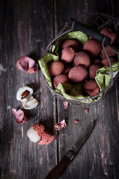 Wire basket, knife and whole and peeled lychees on dark wooden table
