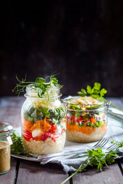 Rainbow salads in jars with quinoa, carrots, peas, red cabbage, bell pepper, mung bean sprouts, the other with tomatoes, mozzarella, spinach, pea sprouts