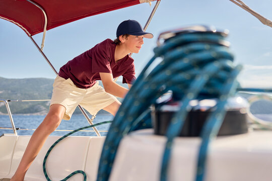 Active boy pulls rope on a sailboat in the ocean during summer