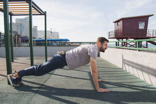 Athletic bearded man performing high plank exercise at outdoor fitness park near seaside strengthening core muscles improving endurance balance healthy lifestyle functional training concept