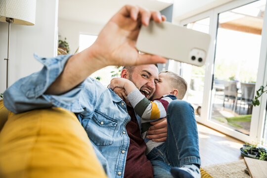 A father and son take a fun selfie with a mobile phone at home