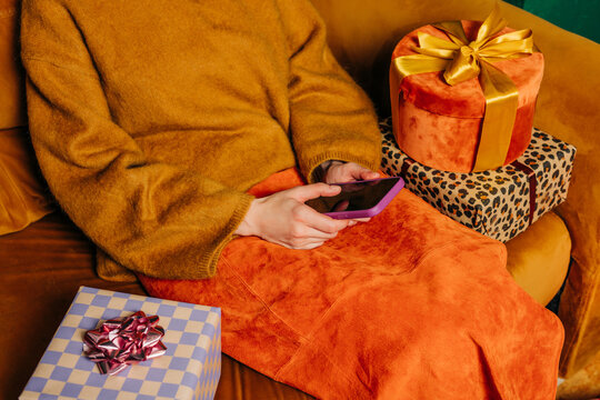 Woman sitting on couch with gifts uses smartphone