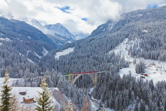 Red train crosses Langwieser Viaduct in snowy Swiss mountains