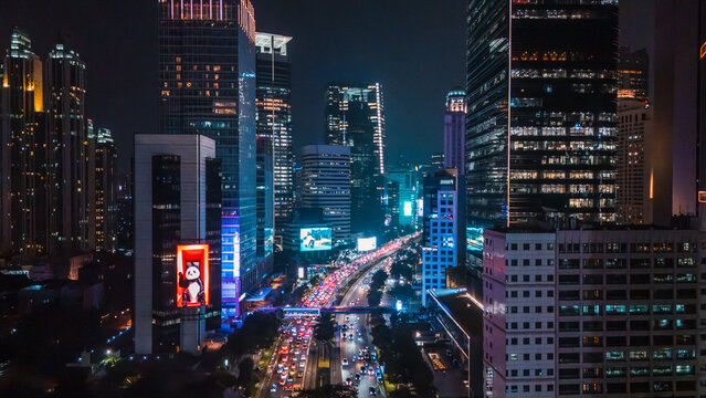 Aerial view of the illuminated Jakarta skyline at night featuring modern skyscrapers, heavy traffic on the highway, and vibrant city lights in Jakarta, Indonesia.