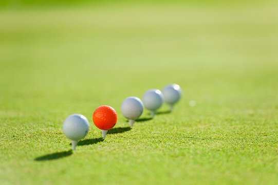 Orange golf ball standing out in a row on a green golf course